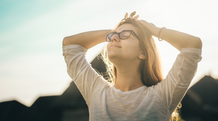Relaxed young woman wearing glasses puts her hands on her head and breathes deeply with her chin up
